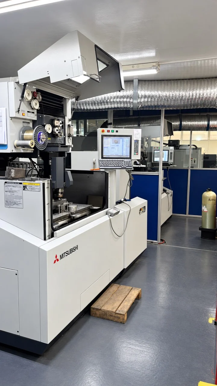 Máquina con alimentación de hilo, zona de trabajo y panel de control, con marca Mitsubishi visible