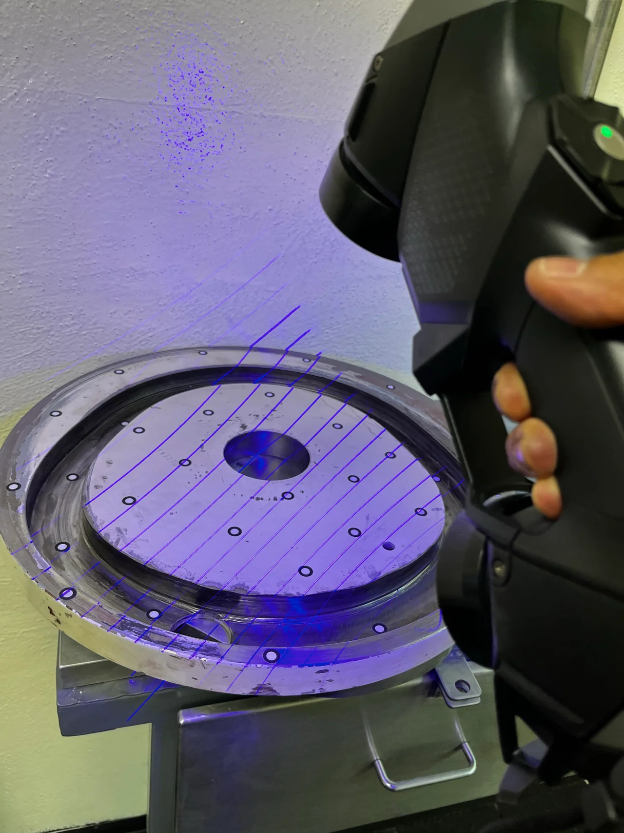 Escáner portátil proyectando líneas azules sobre un componente circular con marcadores